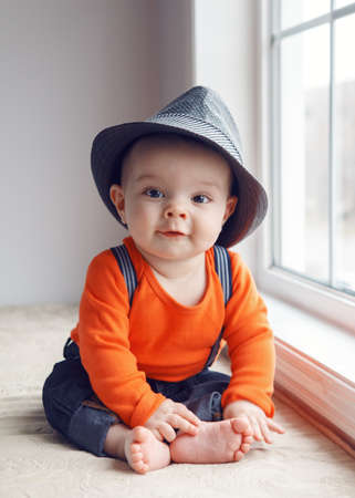Portrait of cute adorable stylish Caucasian baby boy with black eyes in hat, orange shirt  , jeans...
