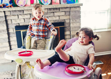 Portrait of cute adorable Caucasian children twins siblings sitting in high chair eating cereal early morning, everyday lifestyle candid momentsの写真素材