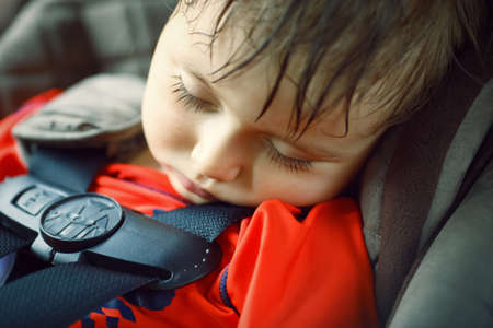 Closeup portrait of a cute adorable little boy toddler tired and sleeping belted in carseat on his trip, safety protection conceptの写真素材