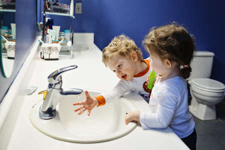 Closeup portrait of twins kids toddler boy girl in bathroom toilet washing face hands brushing teeth with toothbrash playing with water, lifestyle home style, everyday moments, morning routineの写真素材