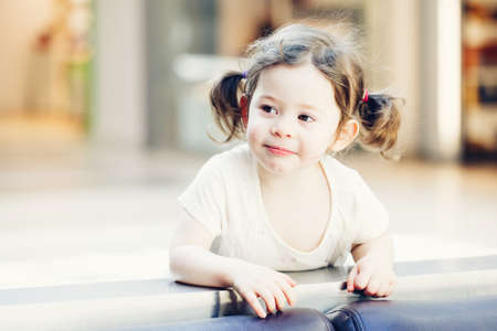 Closeup portrait of cute adorable smiling white Caucasian toddler girl child with dark brown eyes and curly pig-tails hair in white light dress tshirt looking in camera, copyspace for textの写真素材