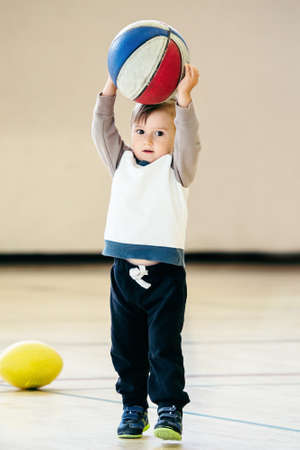 Cute adorable little small white Caucasian child toddler boy playing with ball basketball in gym on plain white light background, having fun, healthy lifestyle childhood conceptの写真素材