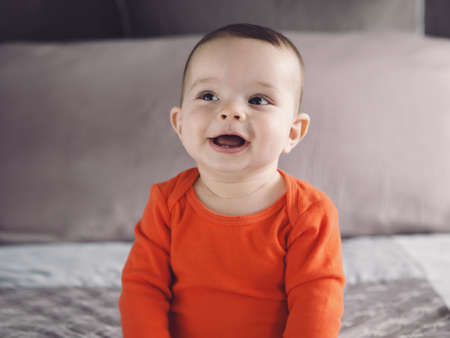 Closeup portrait of cute adorable Caucasian smiling laughing baby boy girl with black eyes in orange...