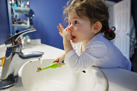 Closeup portrait of  child toddler girl in bathroom toilet washing face hands brushing teeth with toothbrash playing with water, lifestyle home style, everyday moment, morning routineの写真素材