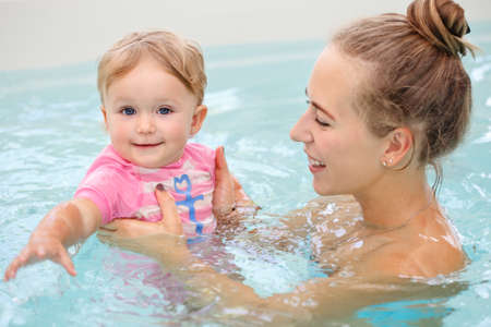 Group portrait of white Caucasian mother and baby daughter playing in water diving in swimming pool...