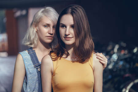 Portrait of two white Caucasian young girls hipster students friends outside on summer day hugging together, selective focusの写真素材