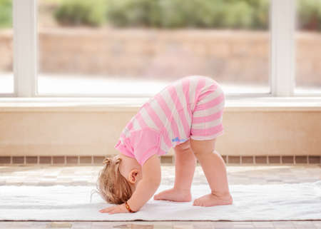 Portrait of cute adorable white Caucasian baby girl doing physical fitness exercises yoga alone standing on floor in swimming poolの写真素材