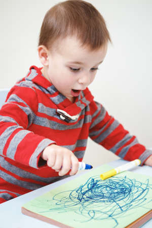 Portrait of cute Caucasian white little boy toddler drawing with color pencils markers on paper in album, looking surprised, excited, mouth open in excitementの写真素材