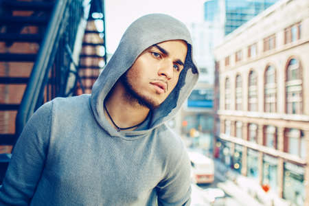 Conceptual art portrait of beautiful handsome gothic young middle east brunette man with blue eyes, beard, wearing blue grey hoodie, outside in urban street looking awayの写真素材