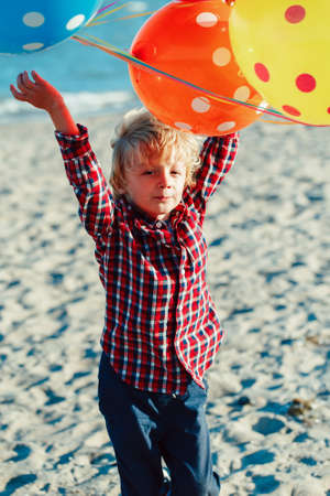 Portrait of funny white Caucasian child kid boy with colorful bunch of  balloons, playing running on beach on sunset, autumn fall seasonの写真素材