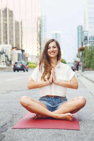 Portrait of slim fit sporty young white Caucasian hippie hipster woman with long blond hair meditating doing yoga exercisers in city streetの写真素材