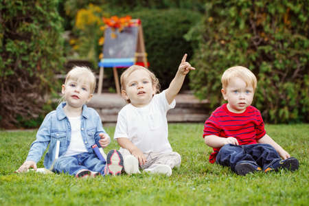 Group of three white Caucasian toddler children kids boys and girl sitting outside in summer autumn park by drawing easel with fall leaves looking in camera, back to schoolの写真素材