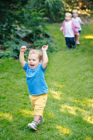Group portrait of three white Caucasian blond adorable cute kids playing running in park garden outside on bright summer spring day enjoying happy childhood lifeの写真素材