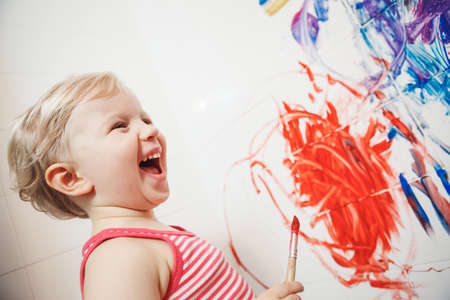 Portrait of cute adorable white Caucasian little boy girl playing and painting with paints on wall in bathroom having funの写真素材