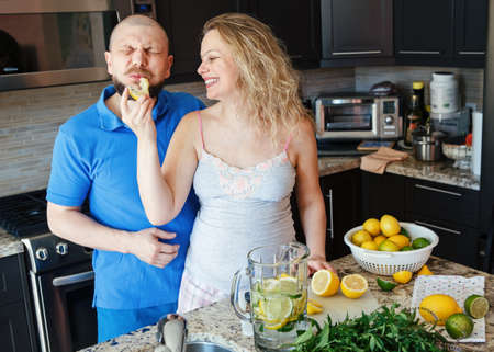 Portrait of smiling laughing white Caucasian couple two people pregnant woman with husband cooking food, eating citrus juice in kitchenの写真素材