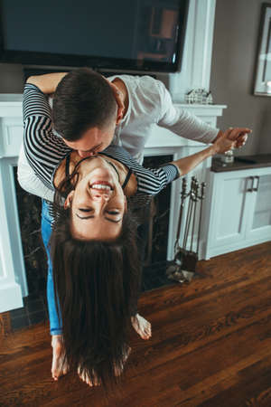 Portrait of beautiful romantic young smiling laughing couple man woman in love hugging, kissing, dancing together indoors at home  in room, toned with filters, authentic candid lifestyleの写真素材