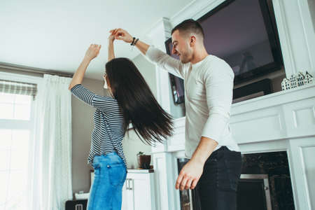 Portrait of beautiful romantic young smiling laughing couple man woman in love hugging, kissing, dancing together indoors at home  in room, toned with filters, authentic candid lifestyleの写真素材