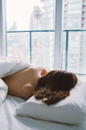 Portrait of young white Caucasian woman lying in bed sleeping, her messy hair on pillow, indoors at home early morning, lifestyle, toned with filters, view from top aboveの写真素材