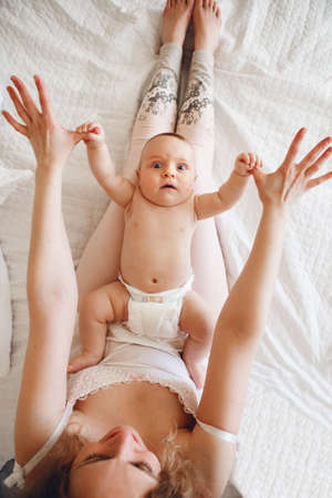 Portrait of  cute white Caucasian newborn baby lying on mother lap doing physical exercises ...