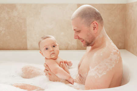 Portrait of white Caucasian middle age father taking bath together with small newborn baby, happy lifestyle candid, daily routineの写真素材