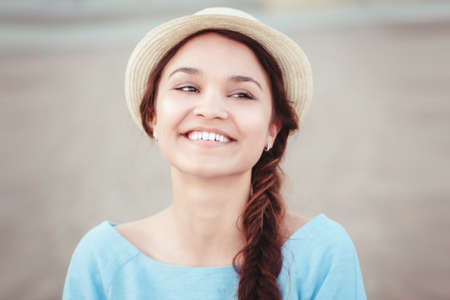 Closeup portrait of beautiful smiling white Caucasian brunette girl with brown eyes and plait in blue dress and straw hat looking in camera rustic retro vintage style conceptの写真素材