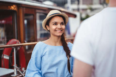 Portrait of beautiful smiling white Caucasian brunette girl on boat yacht pier quay in blue dress and straw hat meeting a male friend, dating hobby lifestyle conceptの写真素材