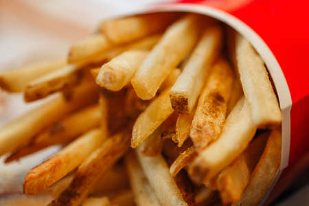 French fries potato chips in red paper cup, closeup macro shot. Unhealthy fried meal in fast food...