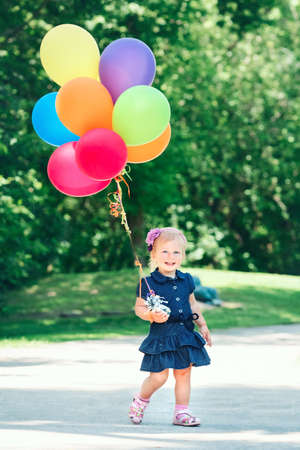 Portrait of cute adorable little Caucasian girl child in blue dress with colorful balloons, in field meadow park outside, happy birthday holiday celebration, lifestyle childhoodの写真素材