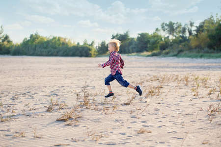 White Caucasian child kid boy playing running on sand beach dunes outdoors on summer day, happy lifestyle childhood concept, copyscpace for textの写真素材