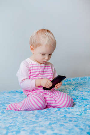 Cute adorable white Caucasian blond baby making a call, playing with mobile cell phone with funny expression on face, lifestyle new generation technology, early developmentの写真素材