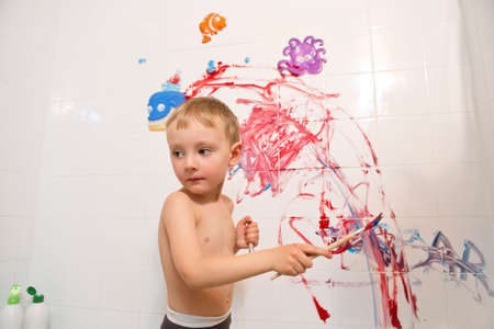 Portrait of cute adorable white Caucasian little boy playing and painting with paints on wall in bathroom having fun lifestyle childhood conceptの写真素材