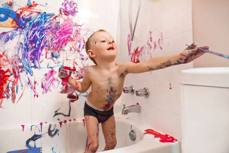 Portrait of cute adorable white Caucasian little boy playing and painting with paints on wall in bathroom having fun lifestyle childhood conceptの写真素材