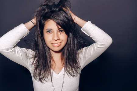 Closeup portrait of beautiful smiling young latin hispanic girl woman with messy long dark hair, brown black eyes, in studio on plain black background,  looking in camera, natural smile emotionの写真素材