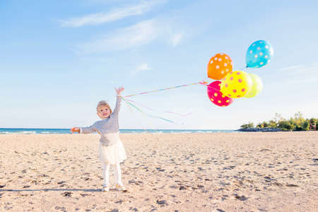 Portrait of cute funny white Caucasian child kid girl with colorful bunch of balloons, playing smiling on beach on sunset, happy lifestyle childhood conceptの写真素材