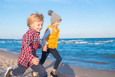 Group portrait of two funny white Caucasian children kids friends playing running on ocean sea beach at sunset, happy lifestyle childhood conceptの写真素材