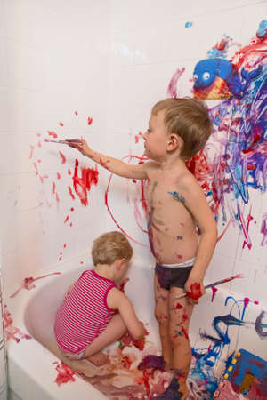 Portrait of two cute adorable white Caucasian little boy and girl playing painting on walls  in bathroom, having fun, lifestyle active childhood concept, early education developmentの写真素材