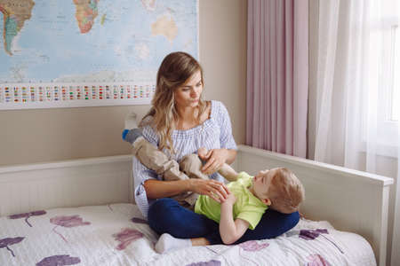 Funny group portrait of beautiful young white Caucasian mother and toddler child boy, playing together on bed in bedroom, having fun, natural candid family lifestyleの写真素材