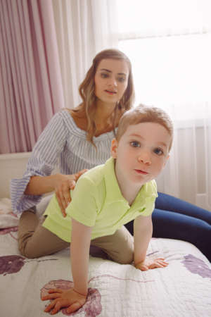 Funny group portrait of beautiful young white Caucasian mother and toddler child boy, playing together on bed in bedroom, having fun, natural candid family lifestyleの写真素材