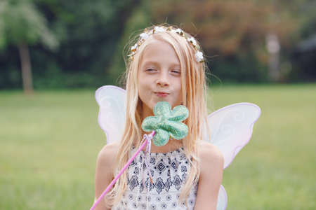 Portrait of smiling blonde white Caucasian child kid girl with long hair wearing pink fairy wings and tutu tulle skirt holding magic wand, happy lifestyle childhood, game play conceptの写真素材