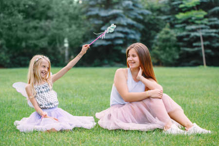 Portrait of two smiling funny Caucasian girls sisters wearing pink tutu tulle skirts in park forest meadow at sunset. Friends having fun together. Girls pretending playing fairies.の写真素材