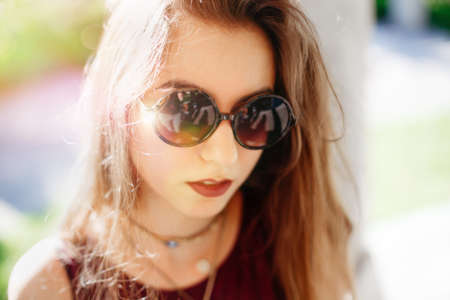 Closeup portrait of beautiful sexy pensive white Caucasian girl woman with long blond red hair, in sunglasses. Hot summer day, lifestyle concept. Sunny day outside, sunbeam leak lighting.の写真素材