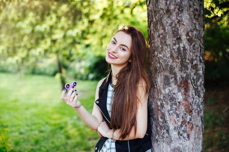 Portrait of smiling white Caucasian young beautiful woman with long hair and brown eyes, playing with fidget spinner toy. Girl holding fidget spinner for stress relief.の写真素材