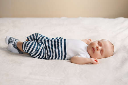 Portrait of sleeping cute Caucasian little baby newborn in white clothes lying on bed with his hands up. Lifestyle candid real concept.の写真素材