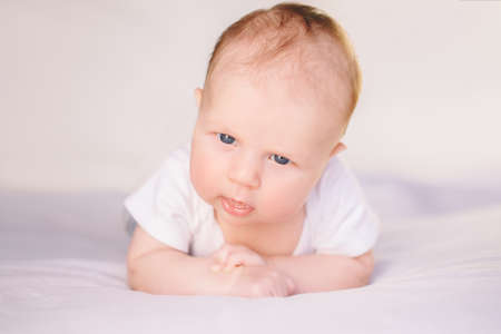 Closeup portrait of adorable funny white Caucasian baby with blue grey eyes lying on tummy belly on...