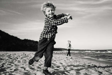 Black and white portrait of Caucasian child kid playing with wooden stick on ocean sea beach on sunset outdoors. Unusual wide angle. Happy lifestyle childhood concept. Natural emotions.の写真素材