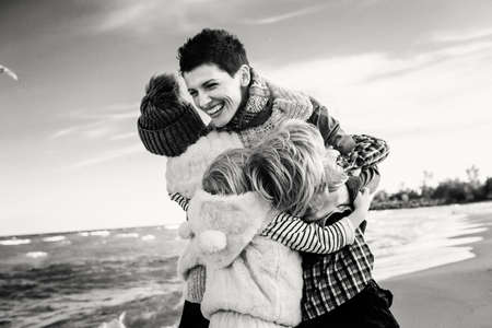 Group black-and-white portrait of Caucasian family mother with three children kids hugging smiling laughing on ocean sea beach on sunset outdoors. Happy lifestyle childhood conceptの写真素材