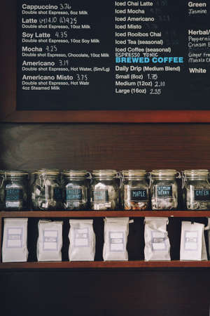 Interior of coffee shop. Wooden board with names of coffee hot and cold drinks, prices. Glass jars with tea bags on shelves. Toned with retro vintage film effect filters.の写真素材