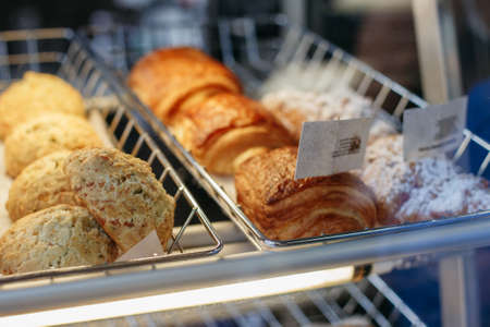 Coffee shop window with baked food, pastries. Closeup macro group of round fresh cheese buns and turnovers in basket with white paperの写真素材