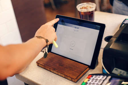 Closeup shot of young caucasian female woman cashier hands. Seller using touch pad for accepting client customer payment. Small business of coffee shop cafeteria.の写真素材