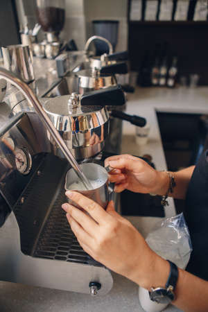 Closeup of Caucasian woman barista hands holding milk jug for making coffee using  coffee machine. Toned with film filters.の写真素材
